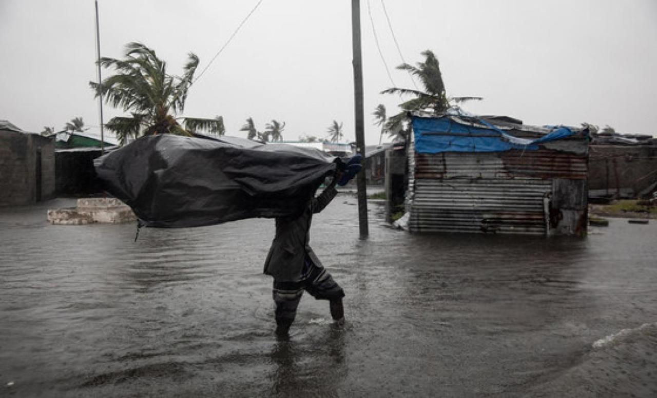 A man walks through the flooded neighbourhood carrying a big black bag above his head.