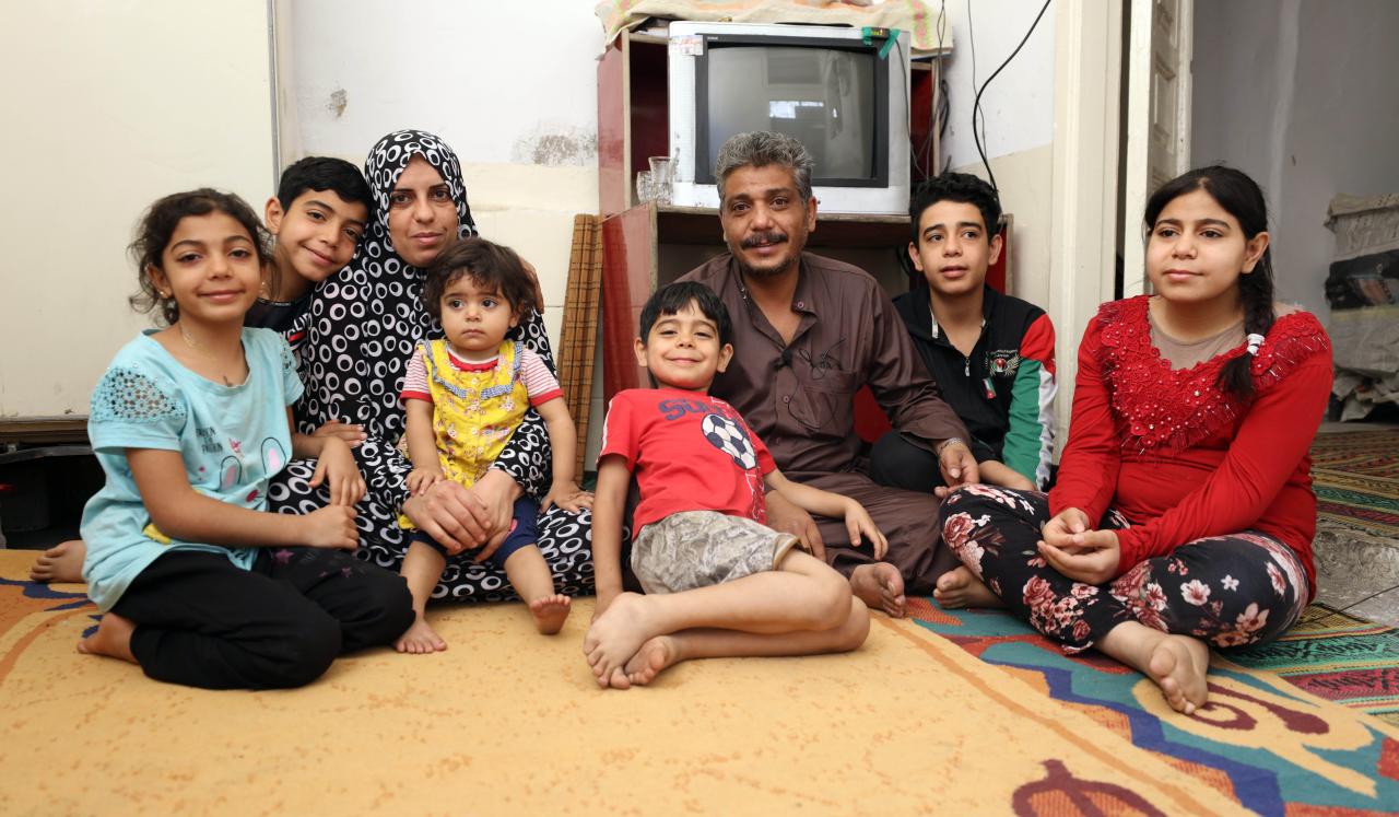 Khaled sits in their tv room on the floor with his family surrounding him.