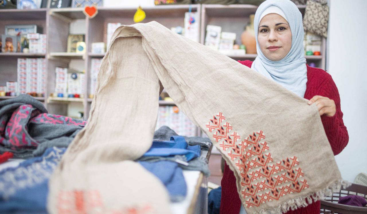 Amal, 33, stands by her work station and holds up fabric.