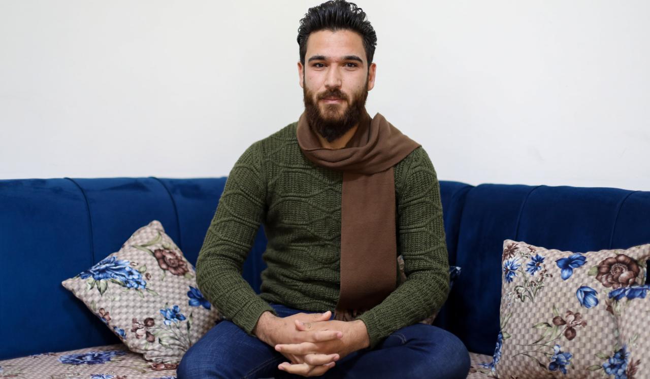 Ammar sits on a sofa with his arms crossed on his lap. 