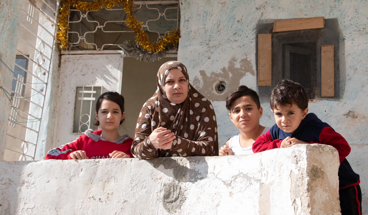 Asma stands with her three children on the porch of their home.