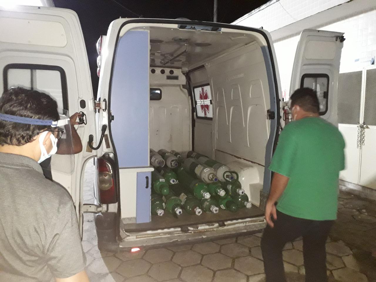 Two men stand near an open trunk of a truck with oxygen tanks. 