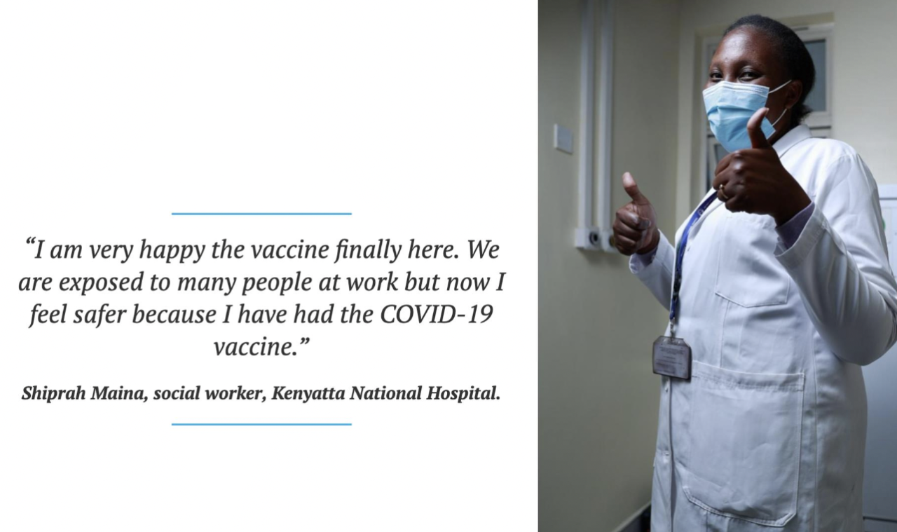 A woman in a white lab coat and blue surgical mask gives the camera thumbs up.