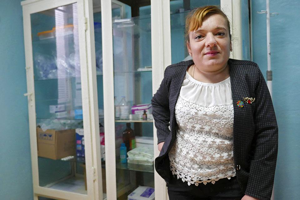 Una mujer con una camisa blanca y una chaqueta negra se encuentra frente a un armario lleno de suministros.