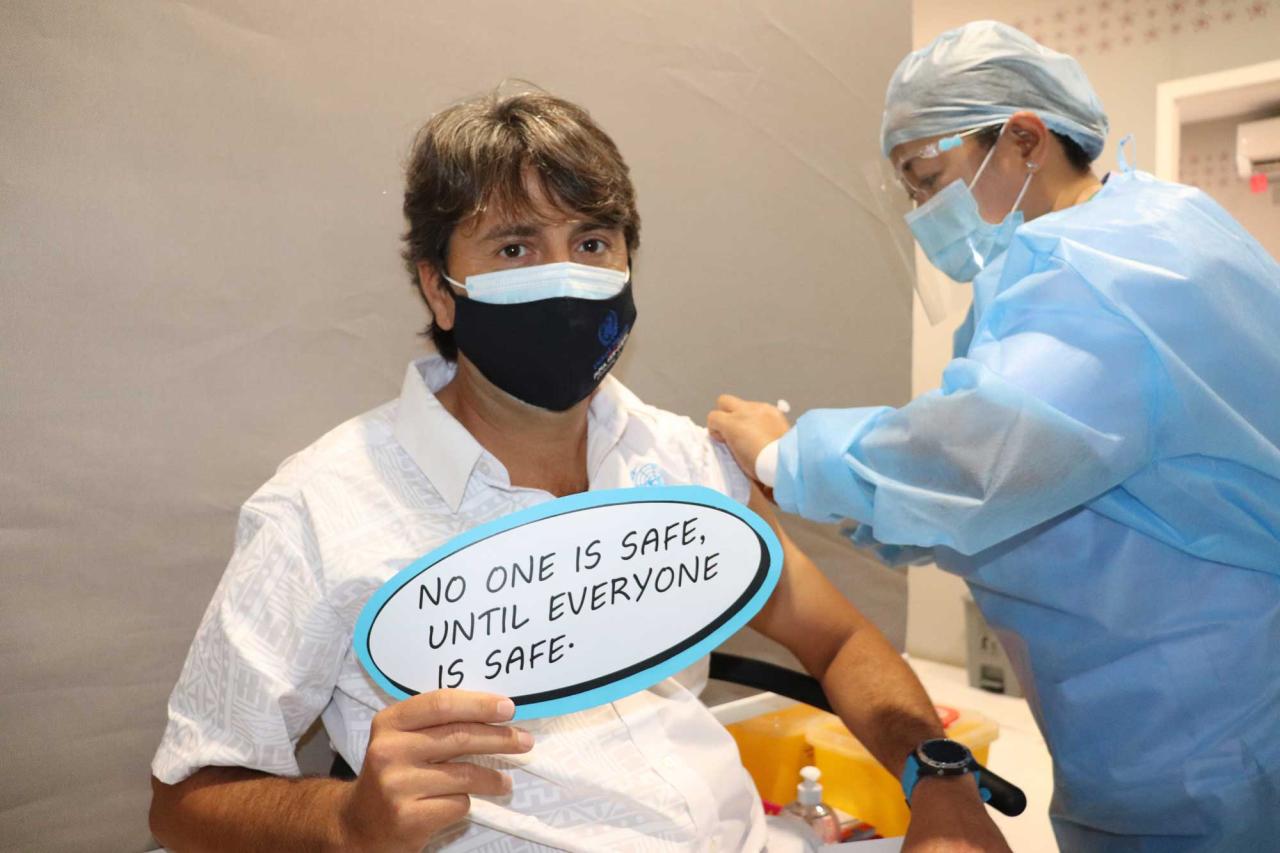 The Resident Coordinator of Papua New Guinea is shown getting his COVID-19 vaccine as he proudly displays a sign noting the safety of the vaccine.