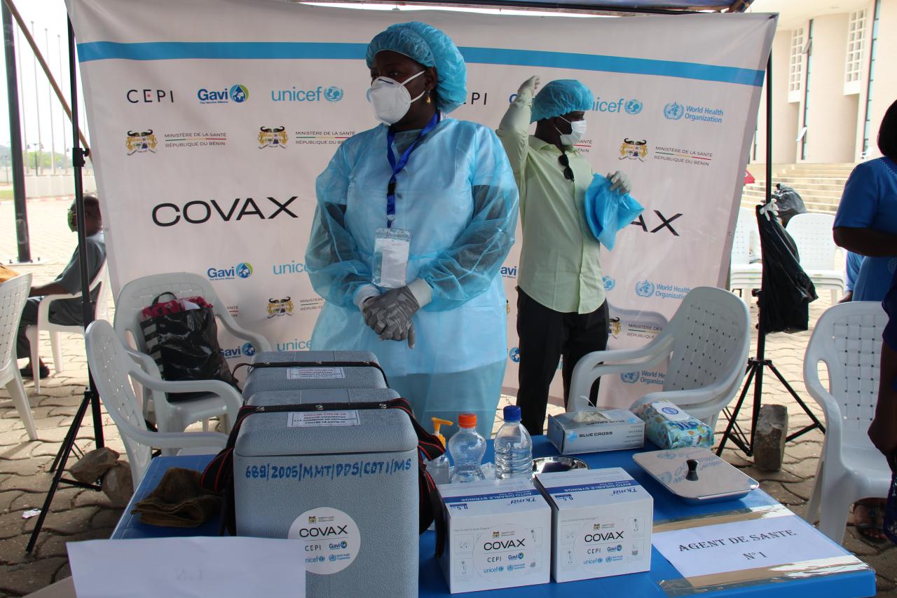 Dos personas con equipo médico de protección se paran cerca de los suministros de vacunación.