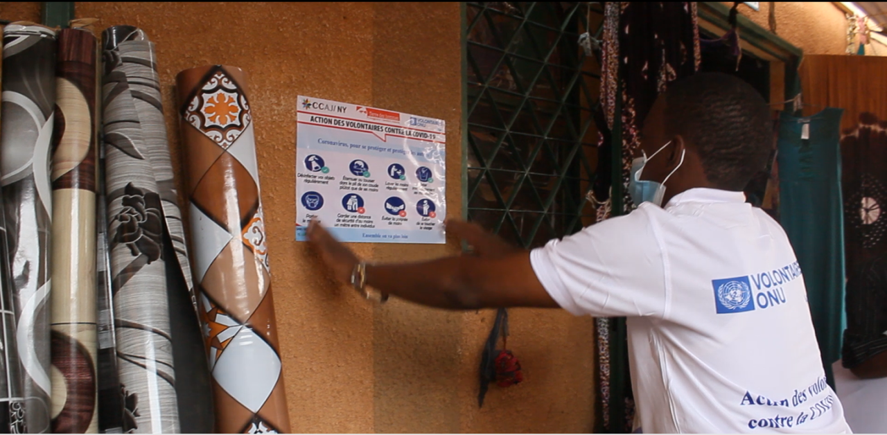A person hangs a COVID-19 informational poster on a wall. 