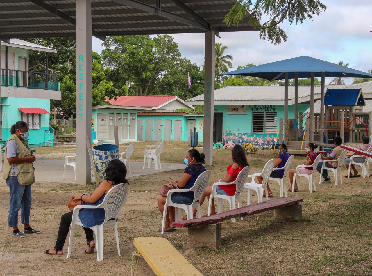 A group of socially distanced women listen to a speaker standing in front of the group.