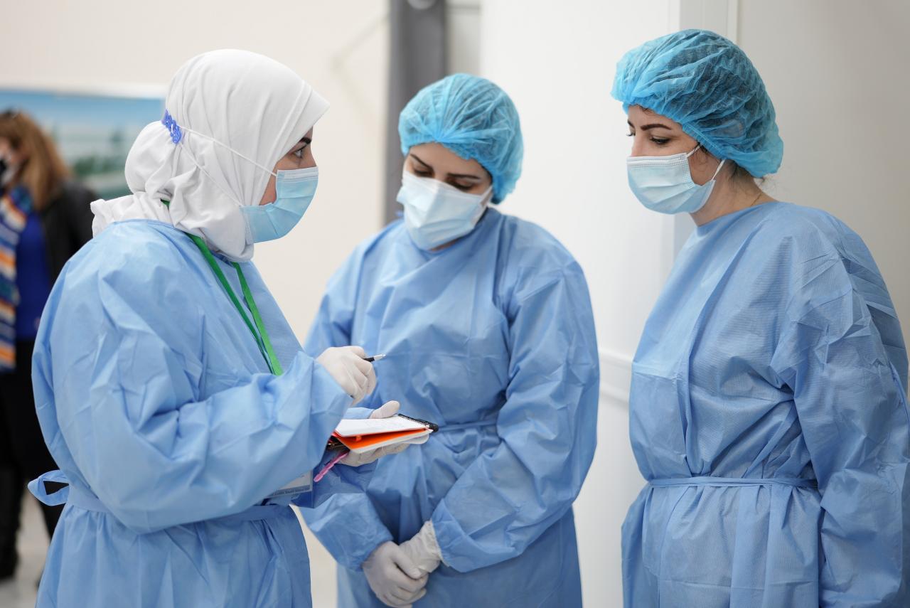 Three people dressed in medical equipment speak in a semi-circle. 