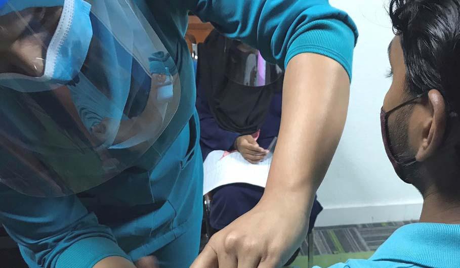 Une homme en tenue médicale et portant un masque et une visière de protection administre un vaccin à un patient portant un masque.