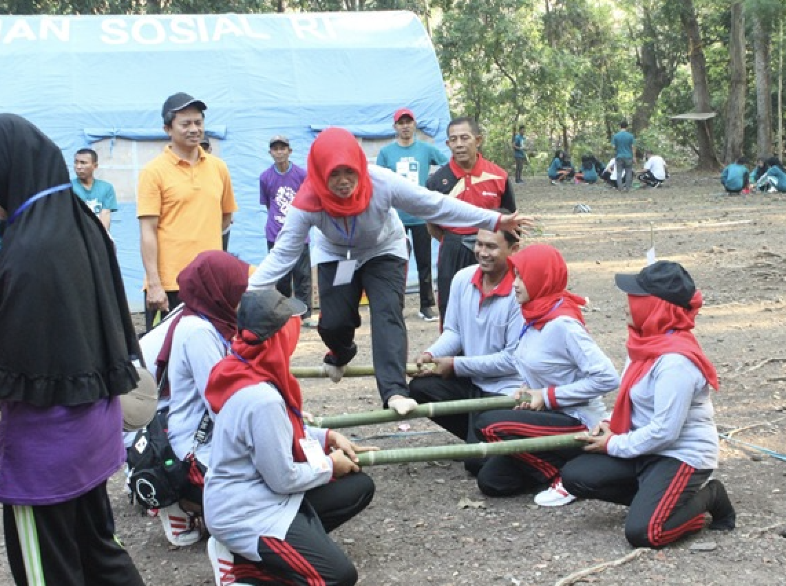 A group of several people play games with sticks in clearing near a wooded area. 