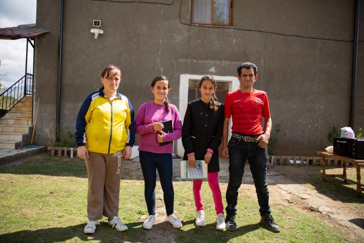 Una familia de cuatro miembros, entre ellos un hombre, una mujer y dos hijas, están parados frente a un edificio.