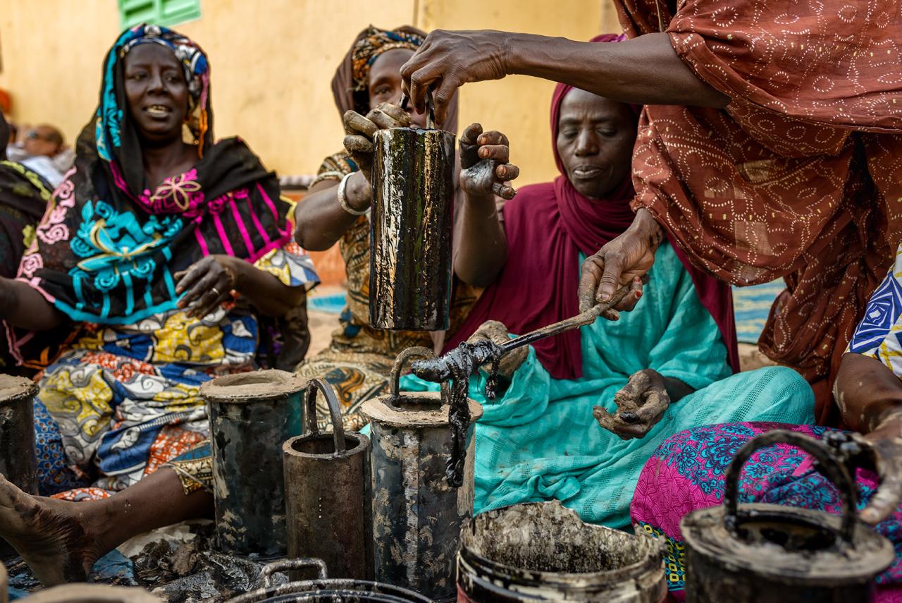 A group of brightly dressed women sit together with pipes. 