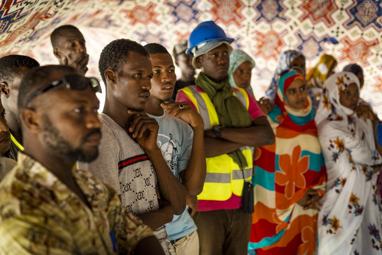 A group of people attentively listen to a speaker who is off camera. 