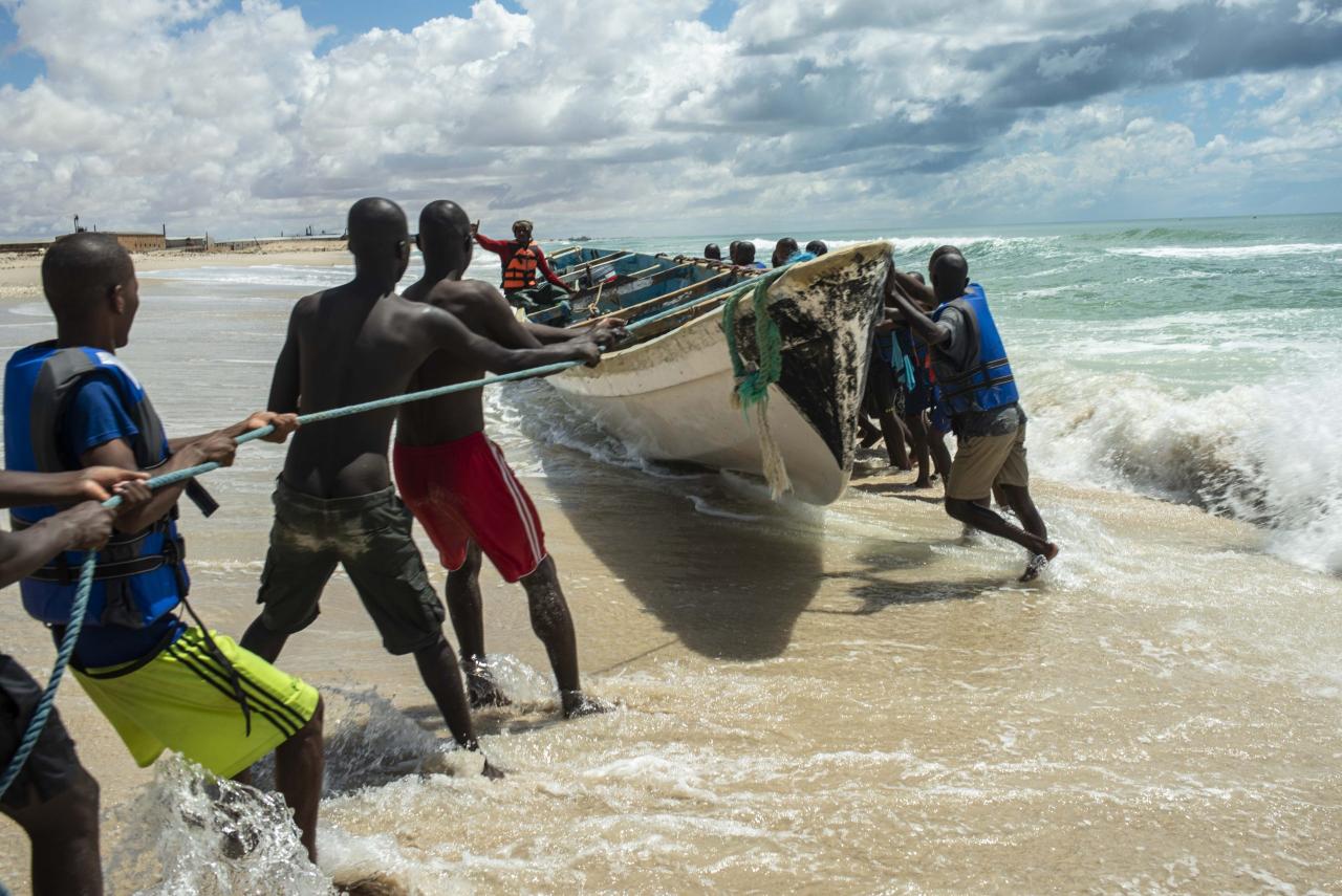 Several people work together to pull out a boat from the ocean. 