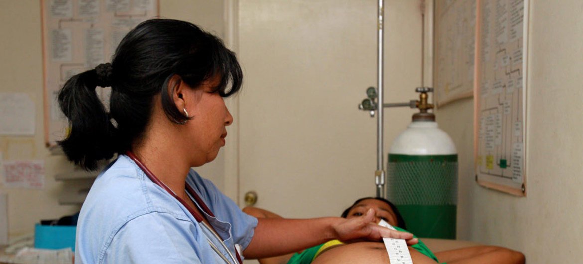 Une professionnelle de santé portant une queue de cheval s'occupe d'une femme enceinte dans un établissement de santé.