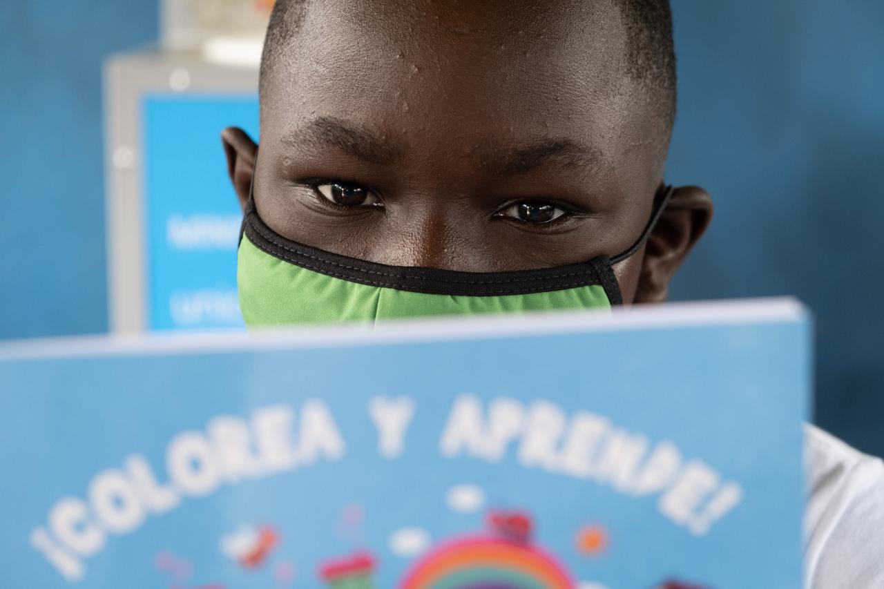 Portrait en gros plan sur une jeune garçon portant un masque de protection respiratoire vert et concentré sur la lecture d'un livre.