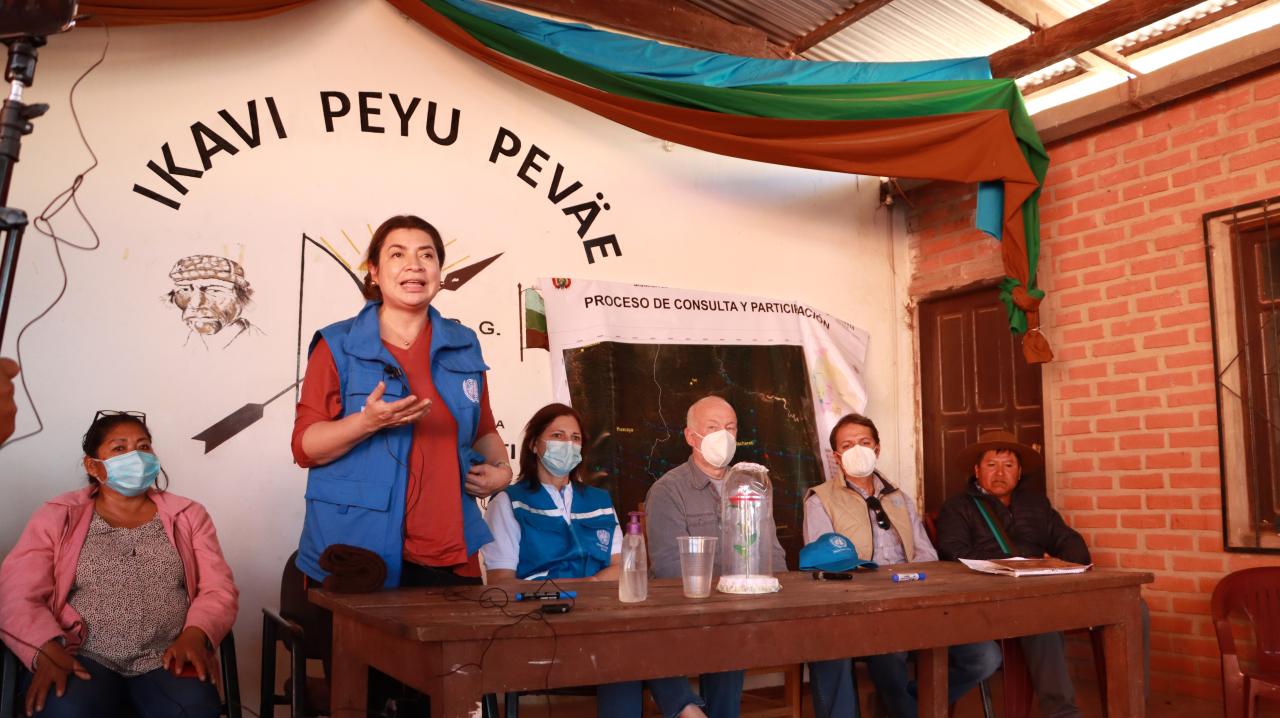 Un grupo de personas con mascarillas sentados frente a una audiencia, mientras Claudia Mojica, Coordinadora Residente de ONU Argentina se dirige a los presentes, durante la visita a la planta de transformación de productos de la agrobiodiversidad en Macharetí Bolivia.