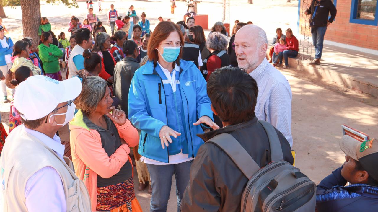 Rodeados de un grupo de personas con mascarillas, Susana Sottoli, Coordinadora Residente de ONU Bolivia y Mario Samaja Coordinador Residente de ONU Paraguay conversan con familias en la comunidad Campo Loa en Paraguay.