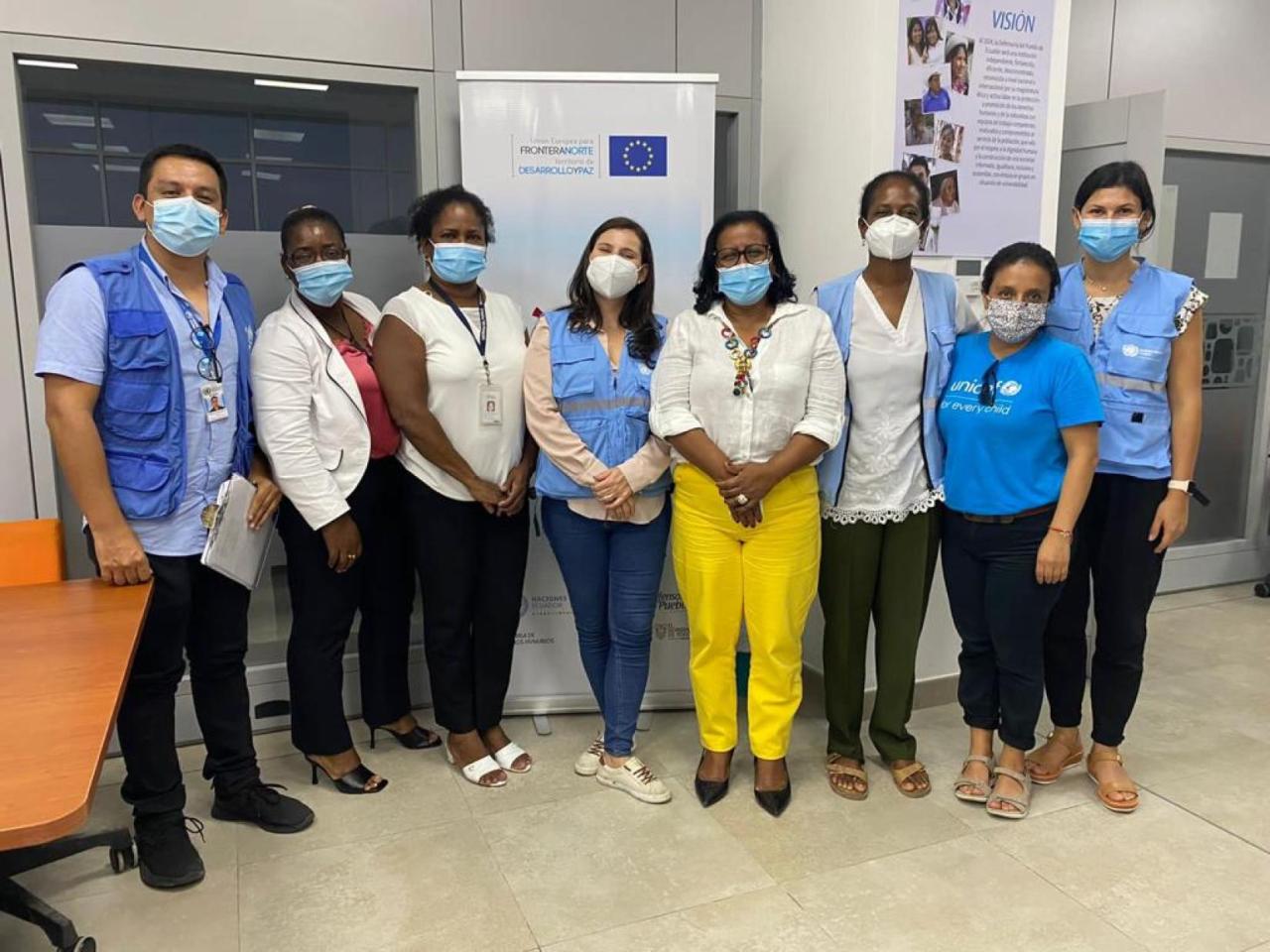 Un grupo de ocho personas de pie, una al lado de la otra, y con mascarillas.
