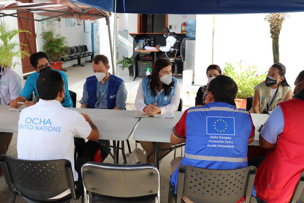 Grupo de personas sentadas alrededor de una mesa: En el centro de la imagen, la Coordinadora Residente Lena Savelli se reunió con colegas de diferentes entidades y organizaciones que trabajan sobre el terreno en Ecuador.