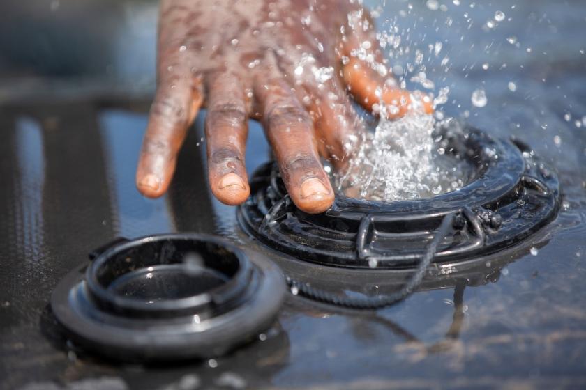 Gros plan sur la main d'un homme éclaboussée par l'eau jaillissant d'un réservoir.