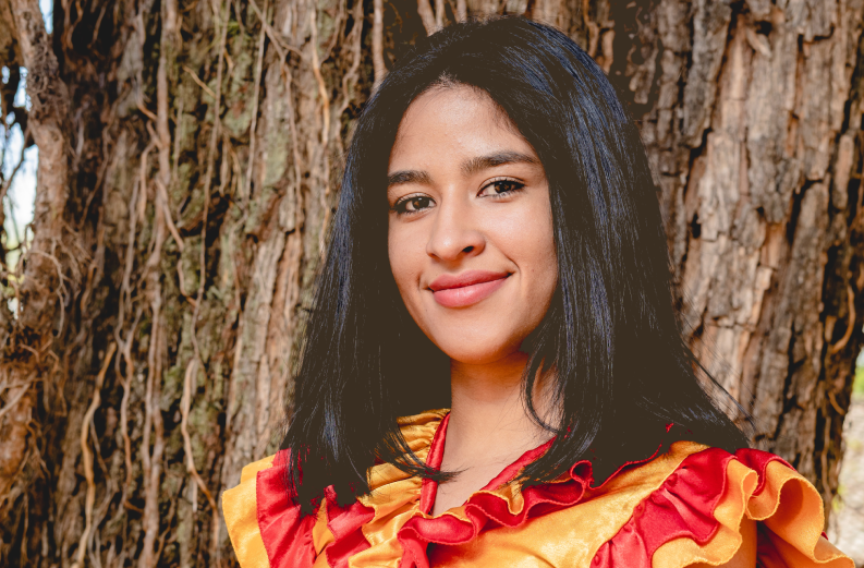 Portrait d'une jeune femme paraguayenne souriante aux cheveux noirs mi-longs et portant un habit traditionnel à volants de couleur rouge. 