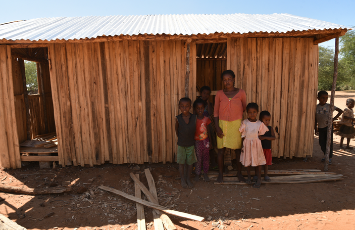 Una mujer malgache se presenta ante la cámara, rodeada de niños y niñas, frente a una humilde casa de madera en la aldea de Amhamahavel, Madagascar.