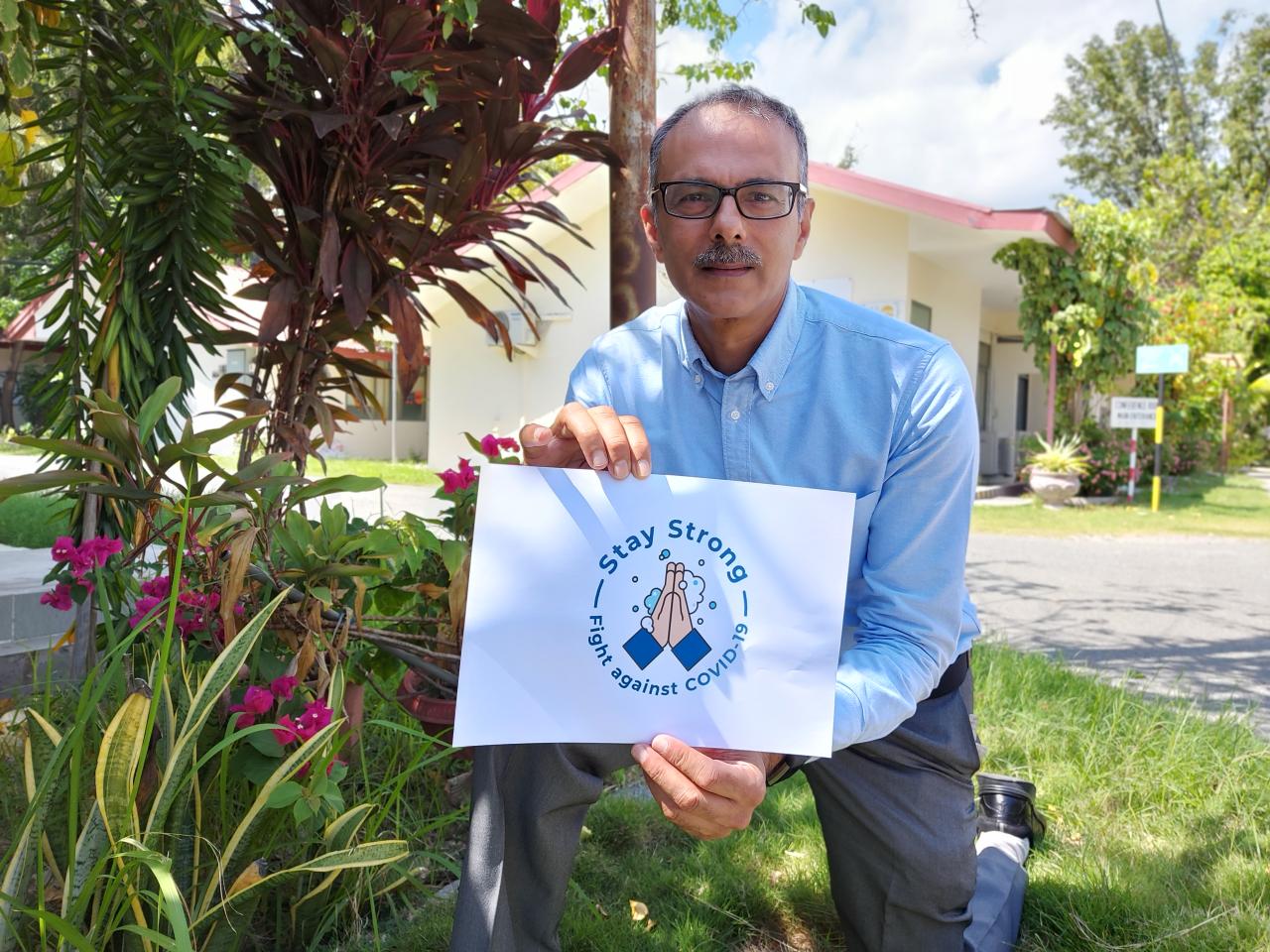 El Coordinador Residente saliente de Timor-Leste, Roy Trivedy, se arrodilla con un cartel para fomentar el lavado de manos durante la COIVD-19.