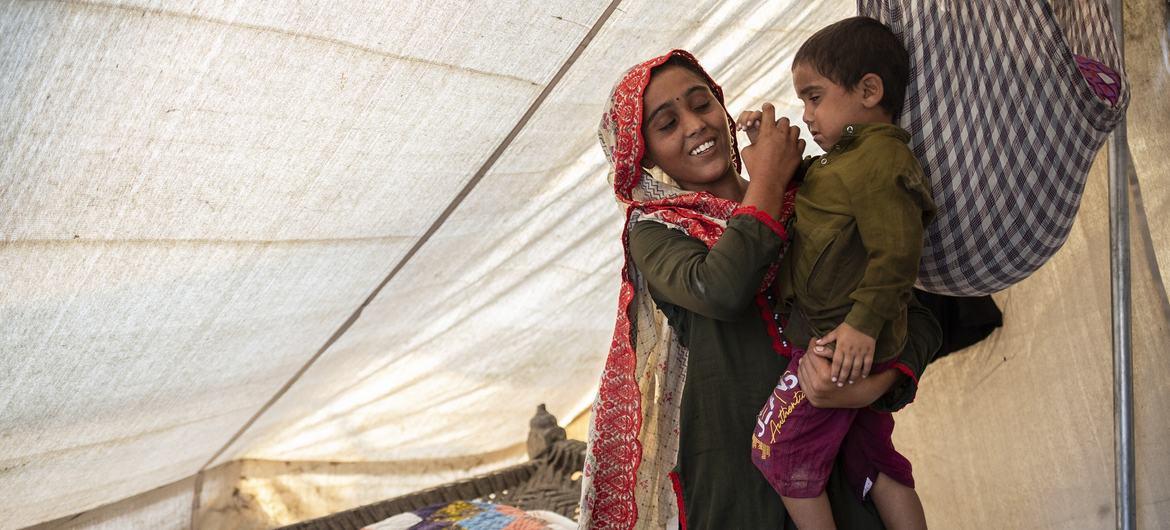 A woman in a tent-structure holds a young boy on her hip. 