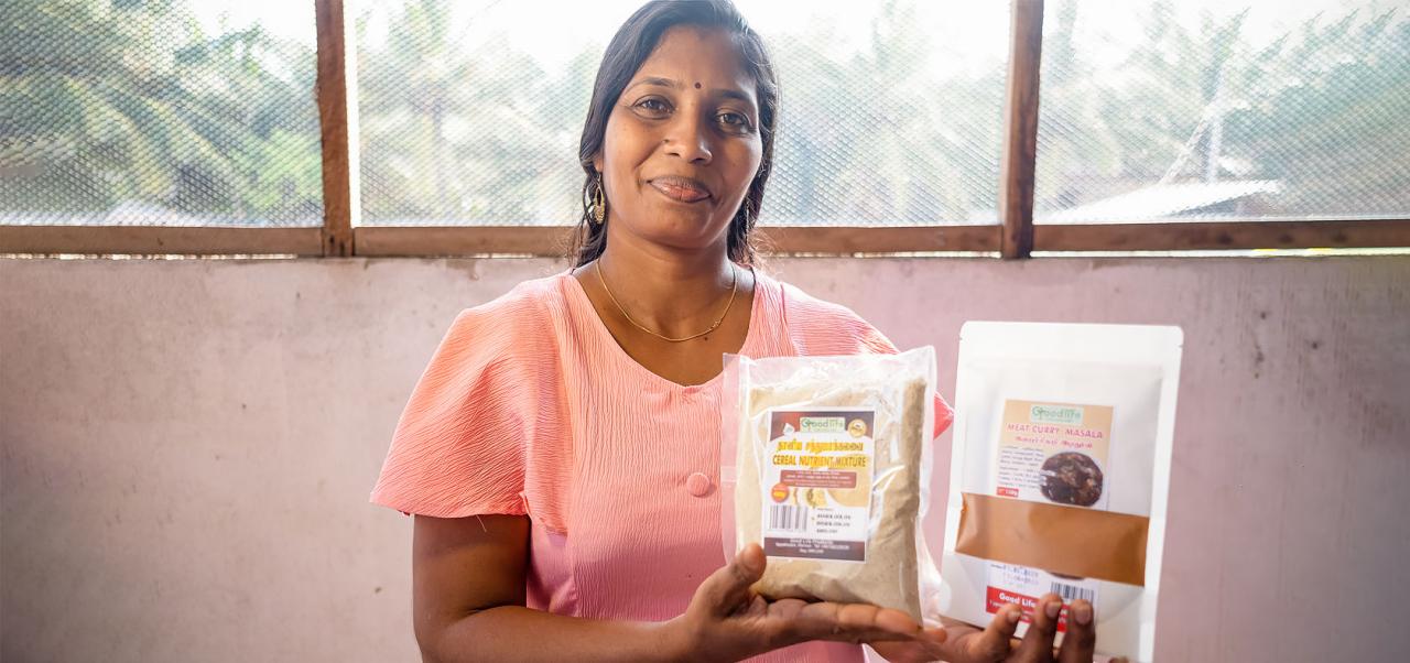 A woman in a light pink top holds some of the products she makes, at her store in Sri Lanka.