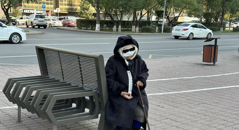 Женщина в повязке на лице и темных солнечных очках сидит на лавочке с тростью в руках