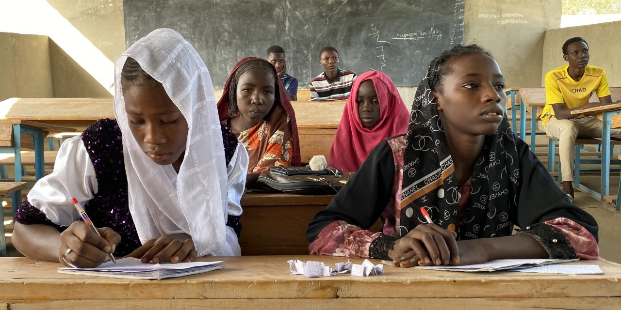 A group of four girls reading and writing on school benches in a classroom