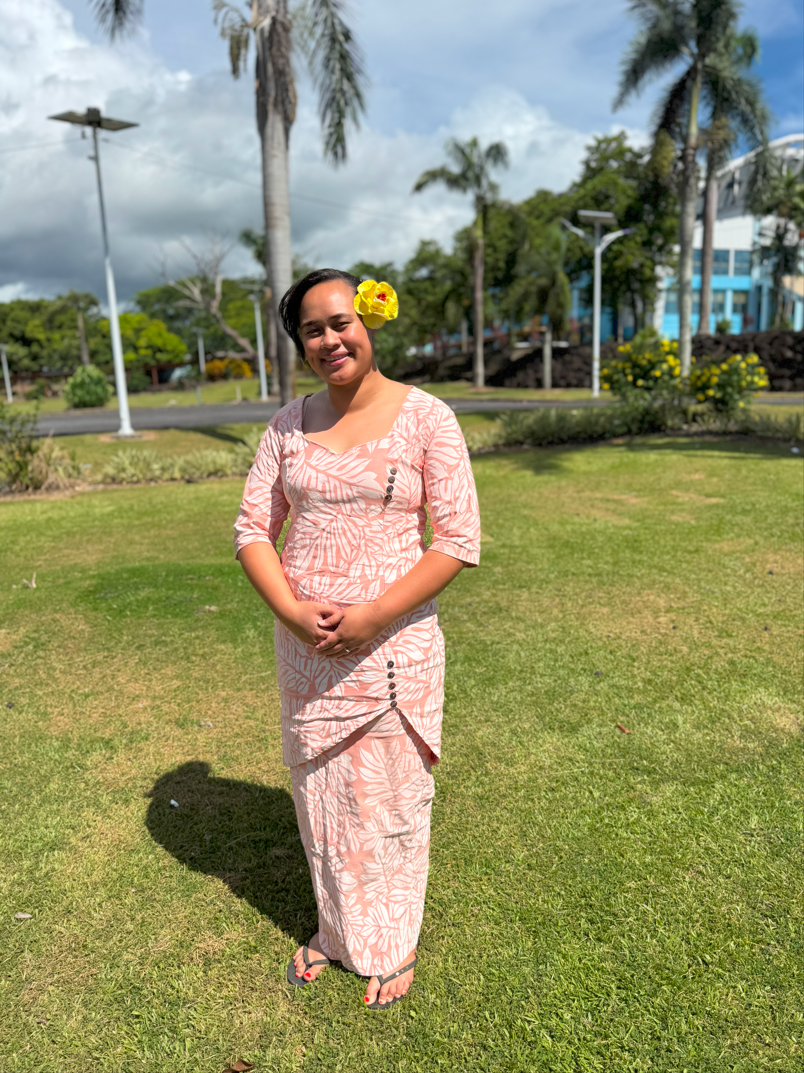 A person wears a colorful dress in front of a green field with trees.