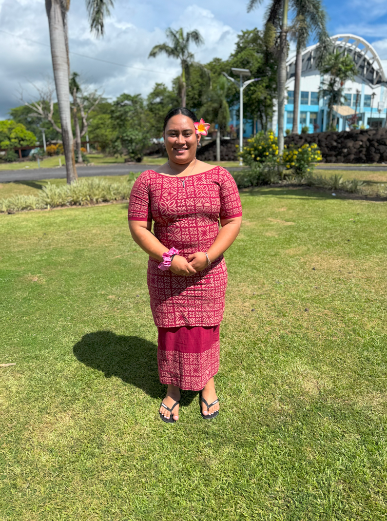 A person wears a colorful dress in front of a green field with trees.