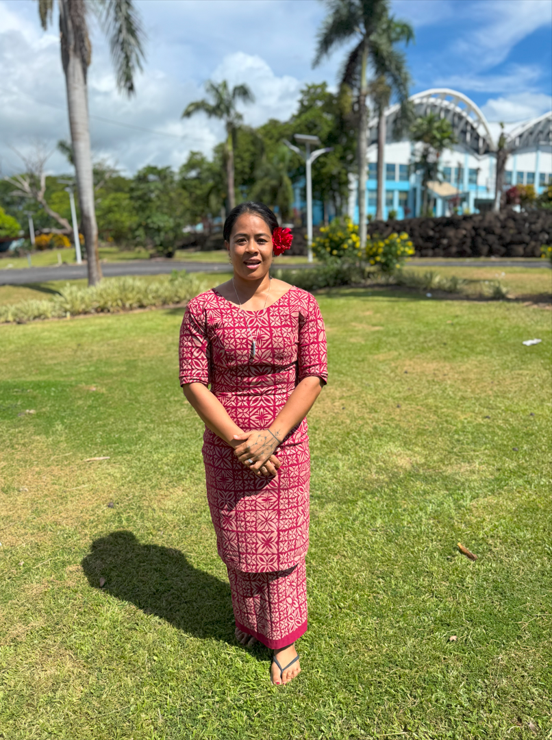 A person in a colorful dress stands in front of a green field with trees