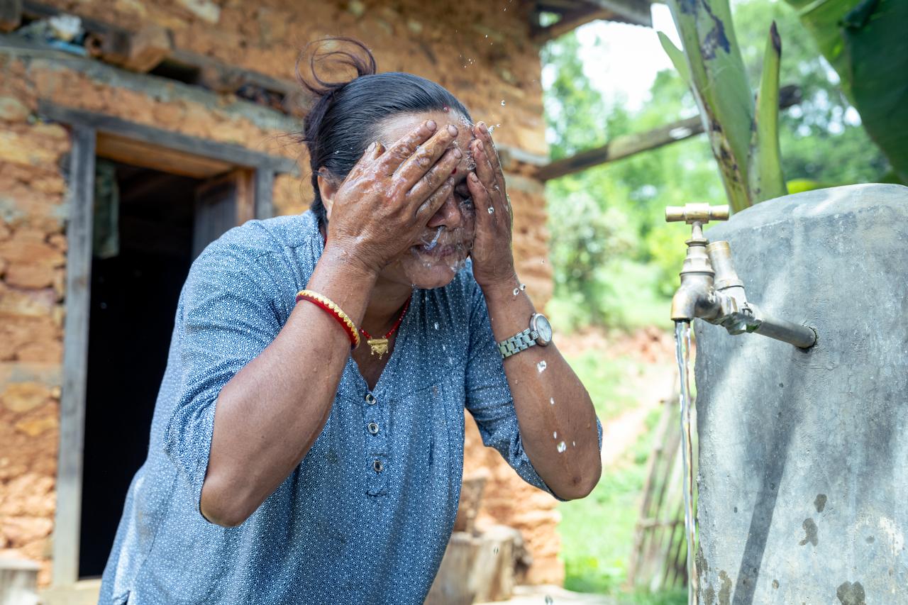 A woman washes her face with water flowing from a pipe