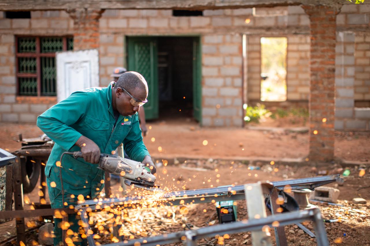 A man in a green suit and goggles fires up an electrical tool as sparks fly.