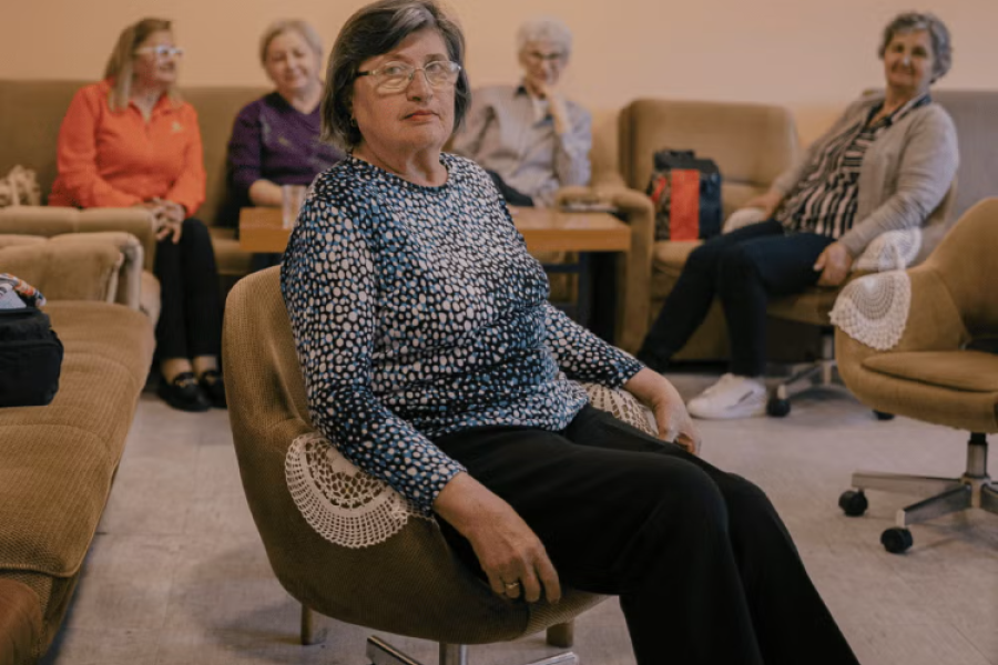 A pensioner in a patterned shirt sits in a brown chair.