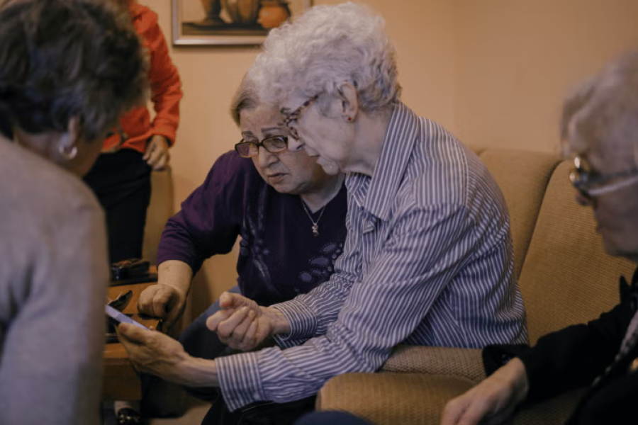A group of pensioners are gathered around a mobile phone.