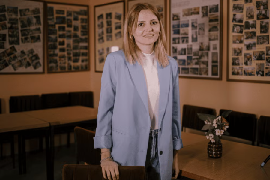A young lady in business casual attire stands and smiles to the camera.