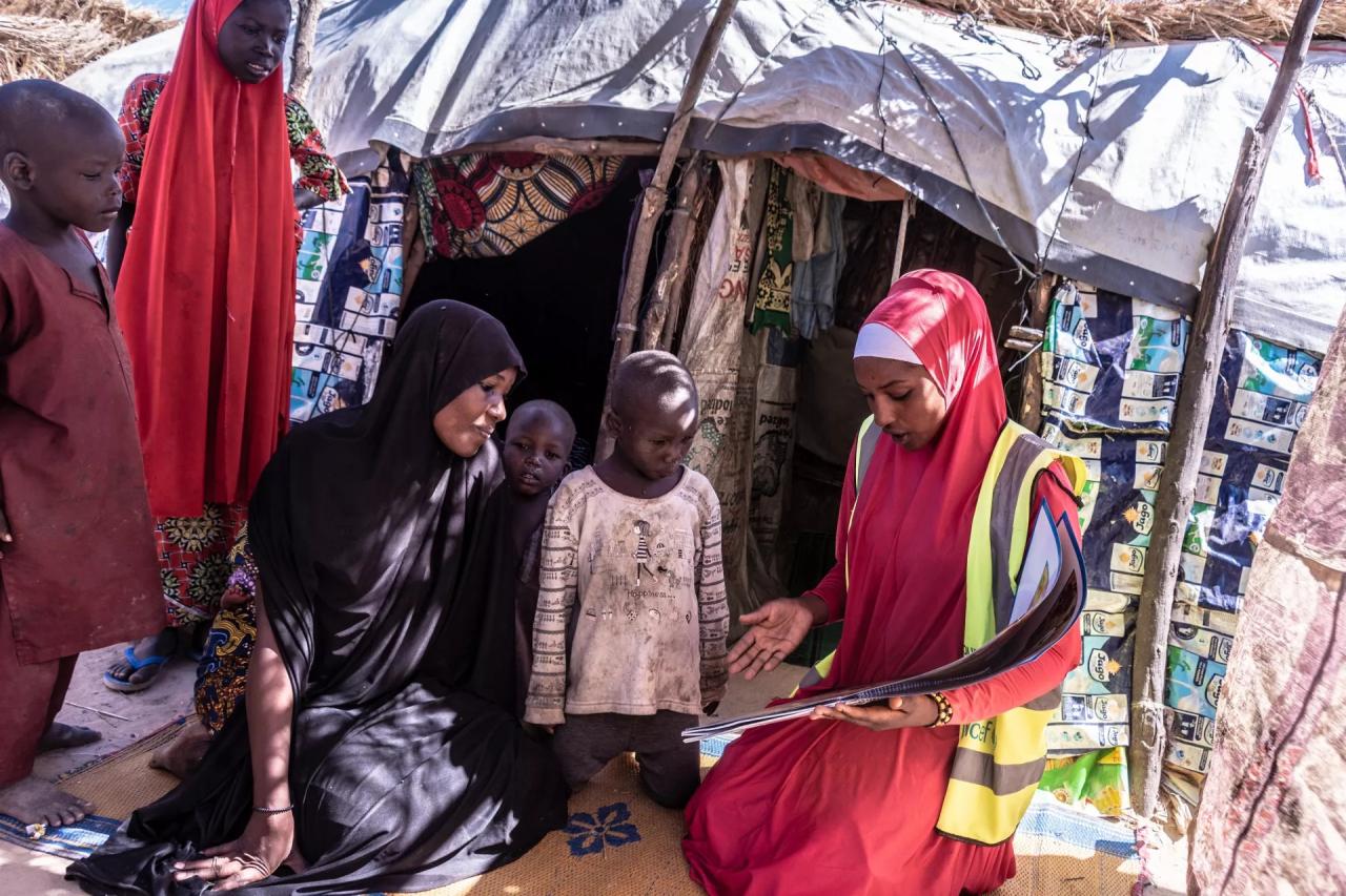 A female volunteer in Nigeria shows a poster to a woman and her four children.