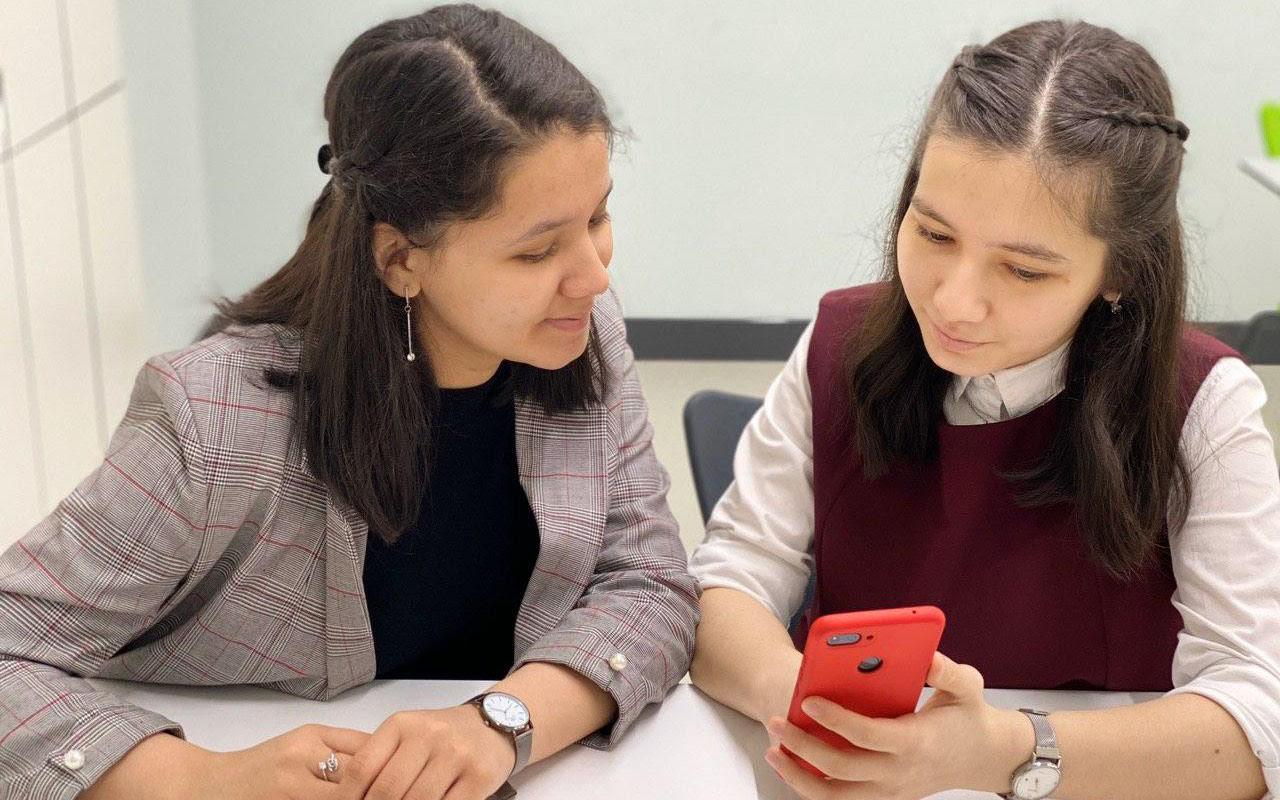 Girl learning to use technology on a phone with her teacher. 