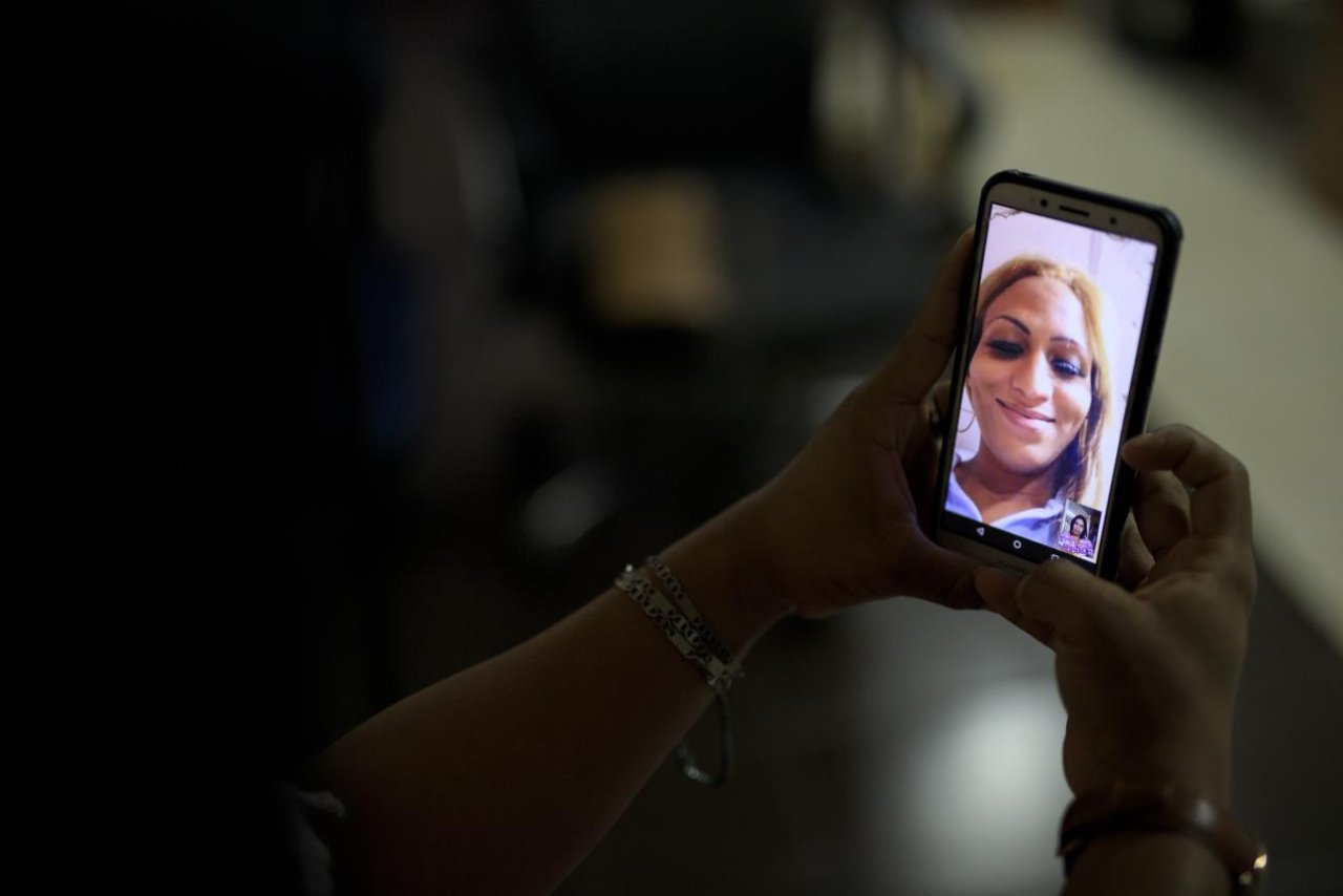 Una imagen de la mano de una persona sosteniendo un teléfono móvil, en el cual aparece la imagen de otra persona, en vio y directo.