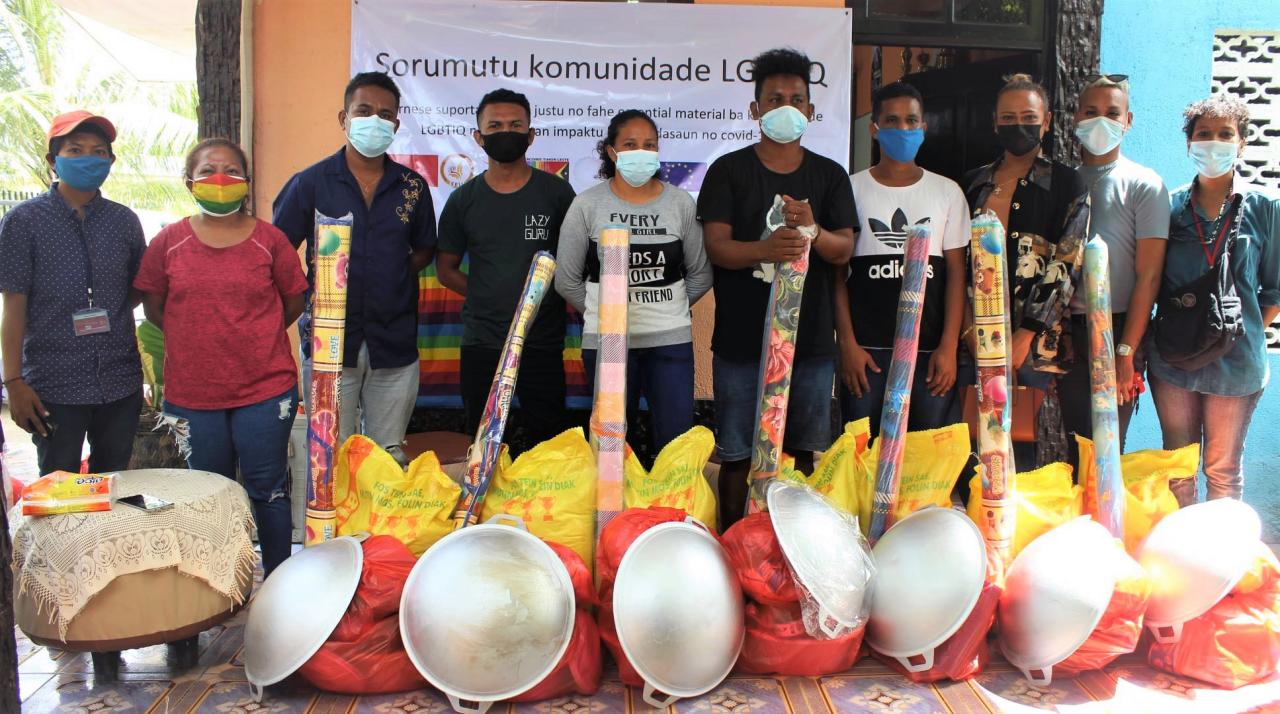 Des membres des équipes d'Arcoiris et de Codiva portant chacun un masque de protection respiratoire se tiennent debout, côte à côte, face caméra, devant des stocks destinés à être distribués aux personnes touchées par le cyclone.