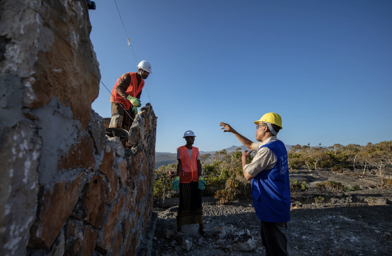 Three construction workers standing near a water tank.