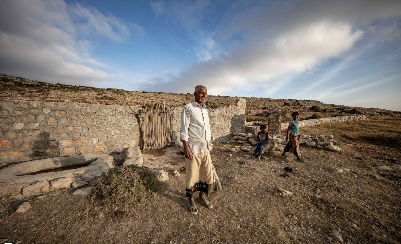 A man stands near a rainwater reservoir with two children standing near him.