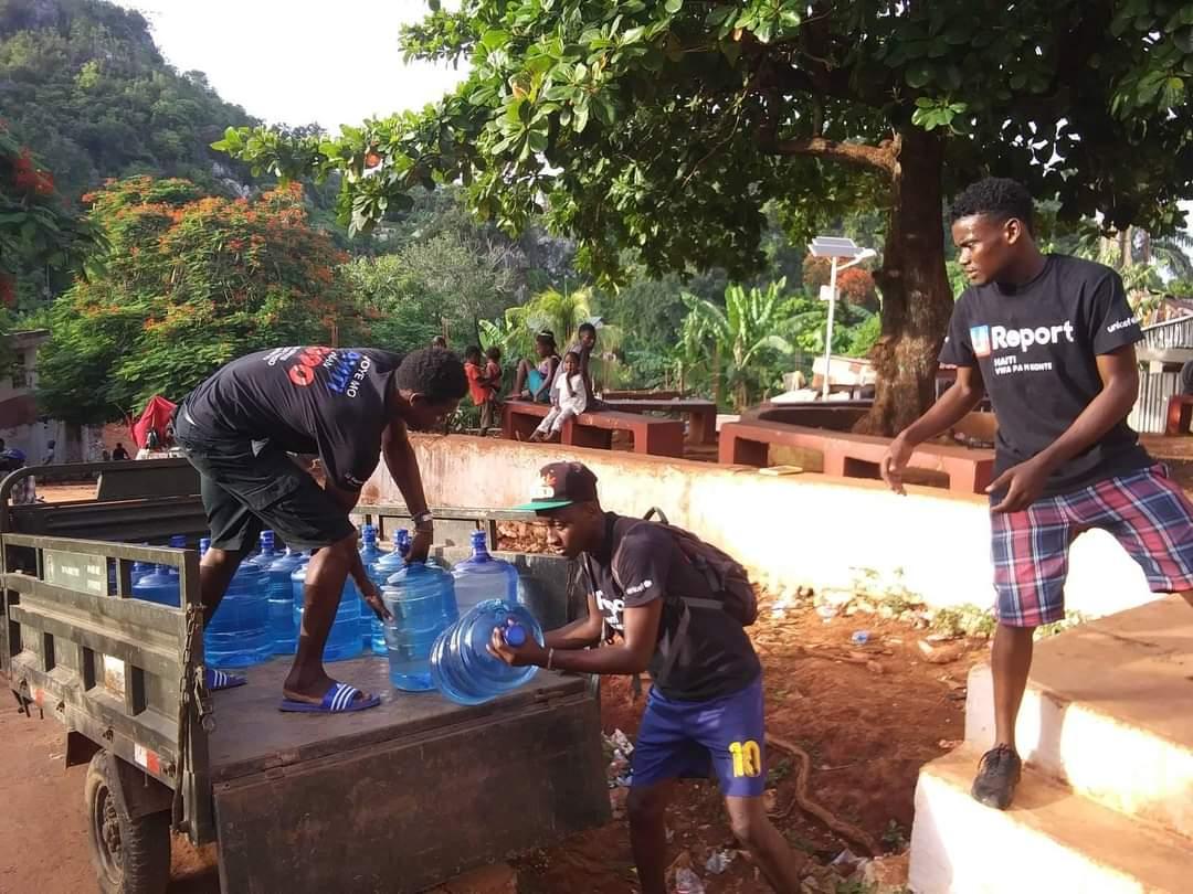 Three people unload large jugs of water from a truck. 