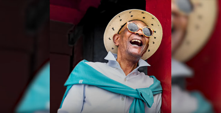 A man in a straw hat and sunglasses laughs.