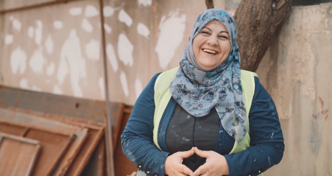 A woman laughs directly at the camera near a partially painted wall. 